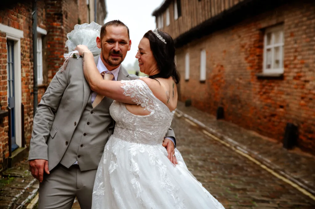 Couple kissing under an umbrella beside a brick wall