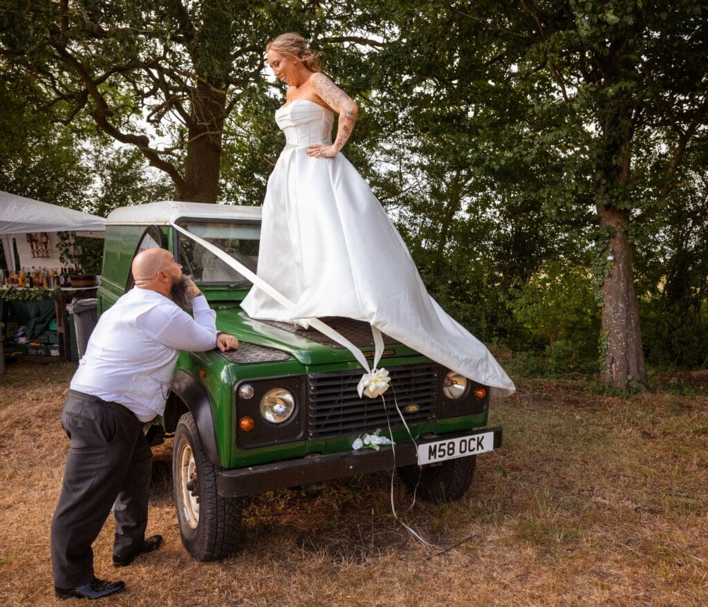 Bride standing on a vintage Land Rover among the trees