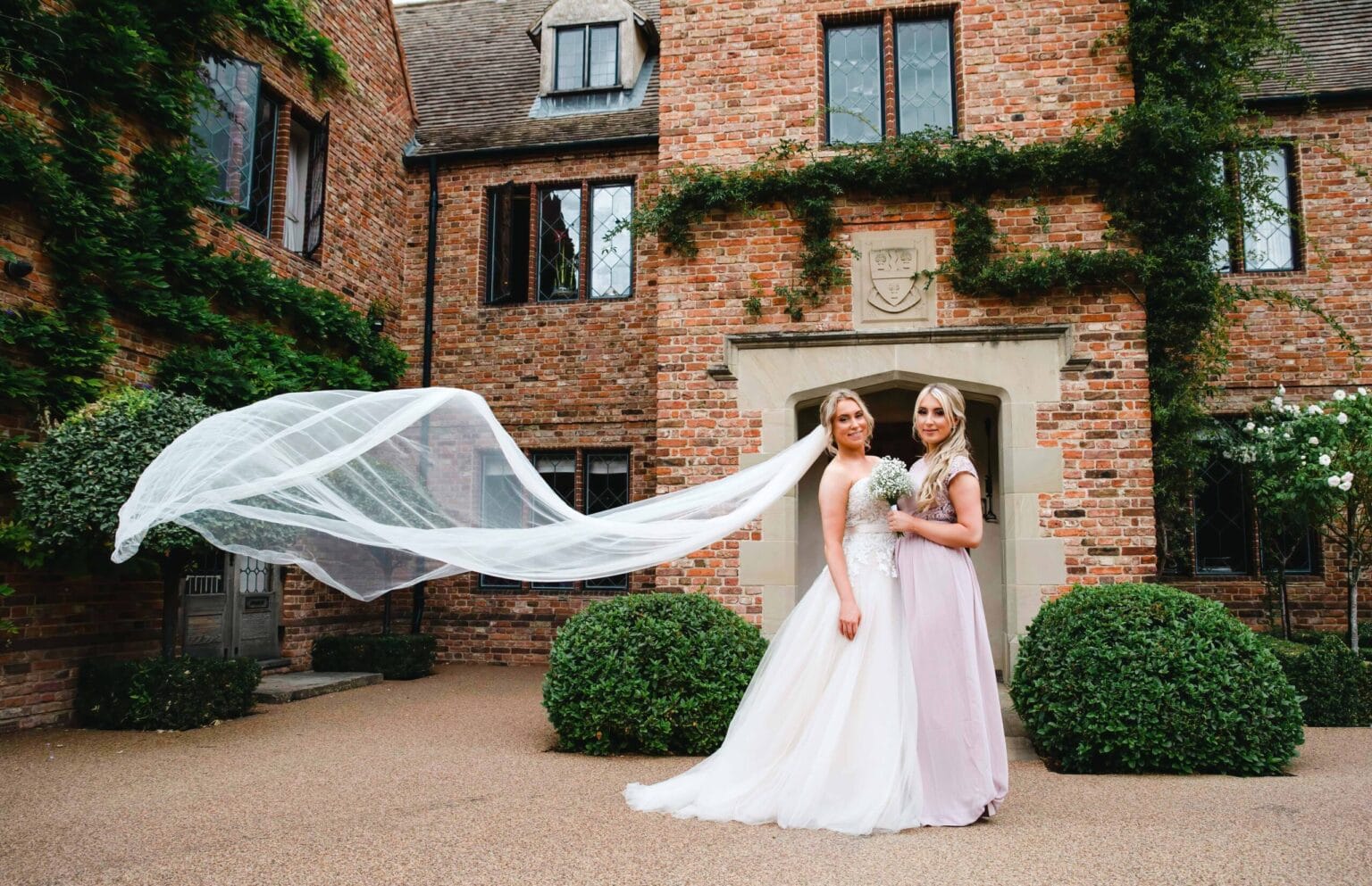 Bride’s veil catching the wind outside an ivy-covered hall