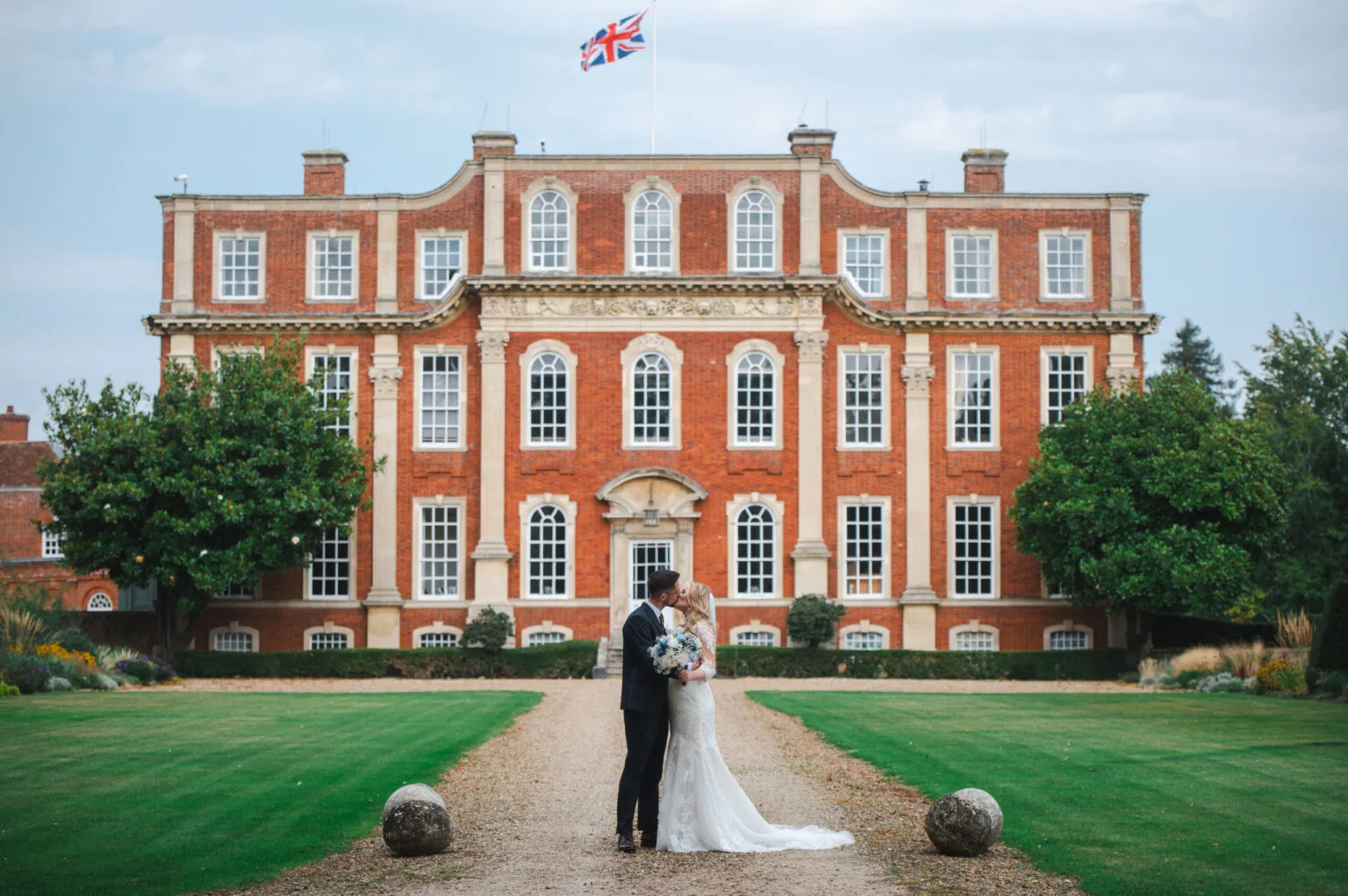 Couple sharing a kiss on the driveway of a red-brick country house